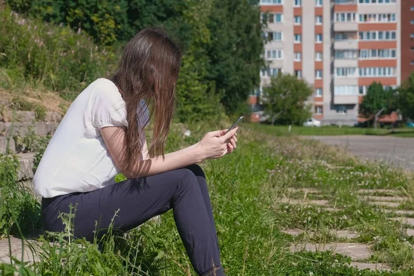 Mujer escribe un mensaje en el teléfono sentado en el parque . — Foto de Stock