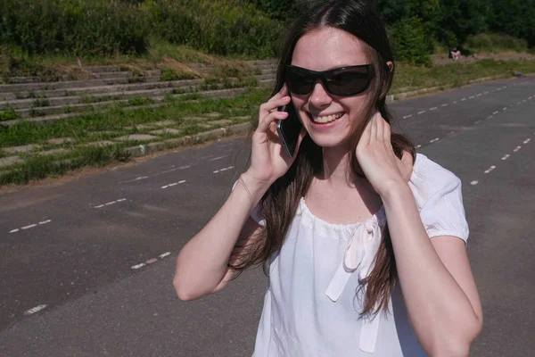 Chica morena joven caminando en el estadio en el parque y hablando en un teléfono móvil . —  Fotos de Stock