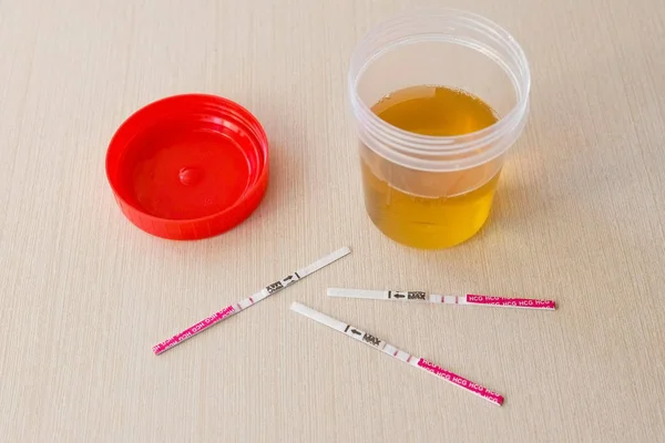 Три положительных результата теста на беременность с двумя полосками на столе. Рядом с банкой с мочой . — стоковое фото