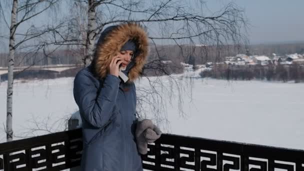 妇女在蓝色羽绒服夹克与毛皮敞篷电话在一个冬天公园她的手机. — 图库视频影像