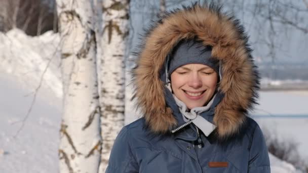 Mujer de cerca con chaqueta azul con capucha de piel fruncida por el sol y sonrisas, en invierno Park — Vídeos de Stock