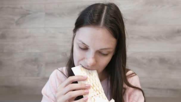Jonge brunette vrouw eten danar of shoarma zitten in een cafe. — Stockvideo
