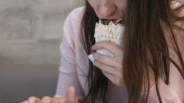 Unerkennbare Frau beim Essen von Danar oder Shawarma sitzt in einem Café und tippt eine Nachricht aufs Handy. — Stockvideo