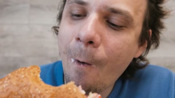 Retrato de un joven comiendo una hamburguesa sentado en un café . — Vídeos de Stock