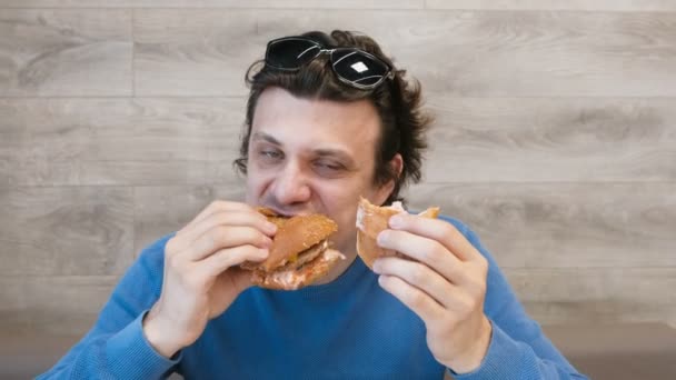 Чоловік їсть гамбургер і шаурму одночасно сидить у кафе . — стокове відео