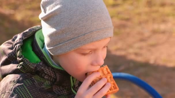 Çocuk parkta bankta oturmuş Waffle yiyor. Yakın çekim yüz. — Stok video
