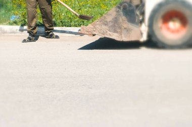 Kent içi temizlik. Adam bir kürekle kir toplar ve her şeyi Ekskavatör kova içine atar. Bacaklar yakın çekim.