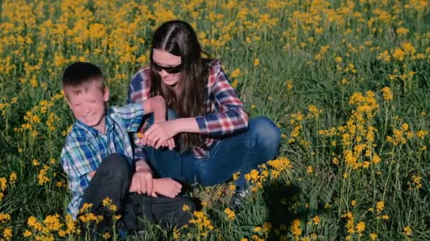 Mãe e filho brincam com flores amarelas sentadas na grama. Excursão familiar . — Vídeo de Stock