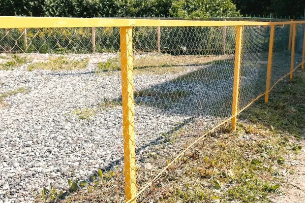 Желтый металлический забор в парке. Огороженная территория покрыта галькой . — стоковое фото