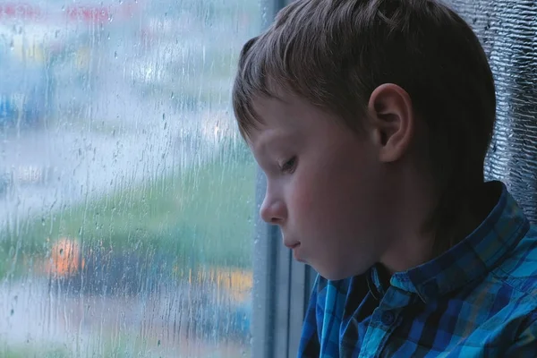 Мальчик смотрит в окно под дождем и грустно . — стоковое фото