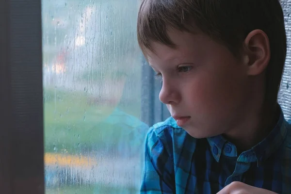 Gutt ser ut av vinduet i regnet og er trist . – stockfoto