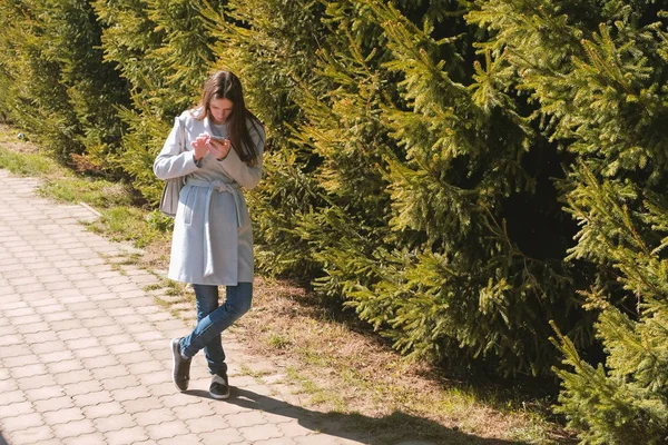 Mujer morena joven en abrigo mira el mapa de navegación en su teléfono para encontrar el camino en la ciudad . — Foto de Stock