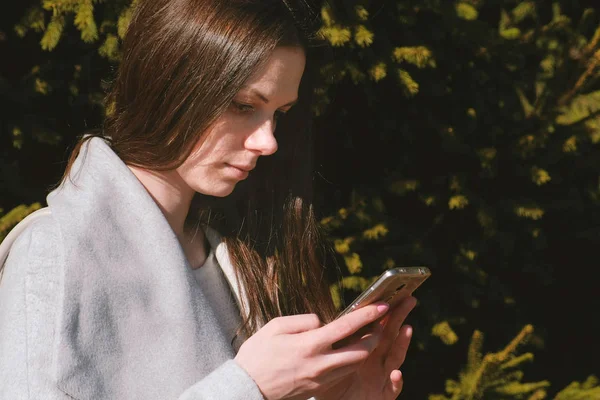 Retrato de bela morena lendo uma mensagem em seu telefone no parque. Vista lateral . — Fotografia de Stock