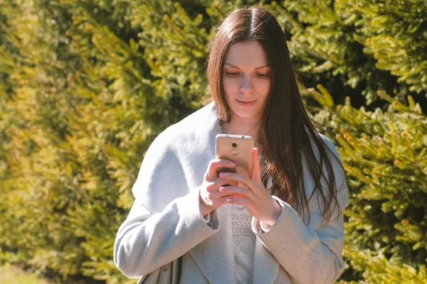 Porträt der schönen Brünette, die eine Nachricht in ihr Handy im Park sendet. Seitenansicht. — Stockfoto