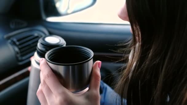 冬に車の中で座っている魔法瓶からカップに熱いお茶を飲む認識できない女性のクローズ アップ ビュー. — ストック動画