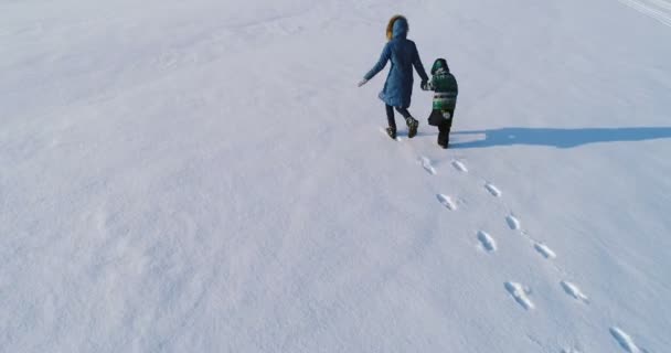 Οικογενειακό χρόνο με τα πόδια και να παίξετε μαζί. Μητέρα και γιος τρέχουν χέρι-χέρι μέσα από το χιόνι που καλύπτει την περιοχή το χειμώνα. πίσω όψη. — Αρχείο Βίντεο