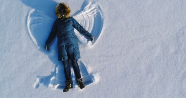 La mujer hace un ángel de nieve tendido en la nieve. Vídeo aéreo . — Vídeo de stock