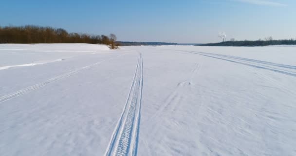 Imágenes aéreas del paisaje invernal de un río congelado con un bosque y una vista de la ciudad con fábricas. Rastros de la moto de nieve en la nieve . — Vídeo de stock