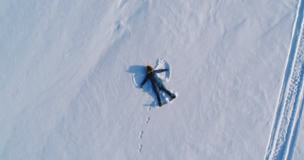 Γυναίκα κάνει χιόνι άγγελος τοποθέτηση στο χιόνι. Εναέρια βίντεο. Κάμερα κινείται αργά μακριά. — Αρχείο Βίντεο