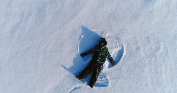 Menino de 7 anos faz anjo da neve, imagens aéreas — Vídeo de Stock