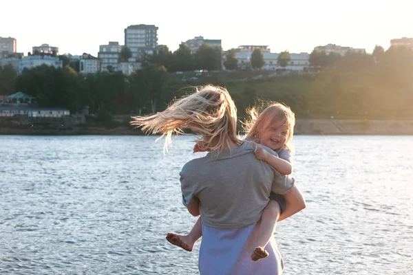 Matka i córka nad rzeką w mieście. Matka z córką na rękach. — Zdjęcie stockowe