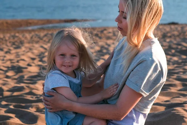 Piękna Blondynka Mama i córka przytulanie na plaży o zachodzie słońca. — Zdjęcie stockowe