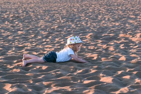 Chica jugando en la arena tendida en la playa . — Foto de Stock