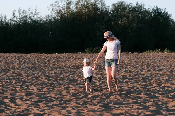 Mama i dziewczyna, chodzenie na plaży nad rzeką o zachodzie słońca w mieście. — Zdjęcie stockowe