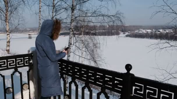 Mujer irreconocible con chaqueta azul escribe mensajes en su celular en Winter Park . — Vídeos de Stock