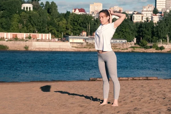 Şehrin nehir kenarında kumsalda Yoga esneme kadın. Harika bir manzara. — Stok fotoğraf