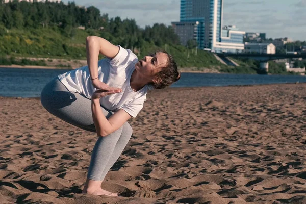 市内の川のビーチでヨガのストレッチの女性。美しいシティー ビュー。Utkatasana ポーズ. — ストック写真