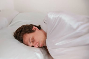 Adam battaniyenin altında yalnız yatakta uyuyor. Yan görünüm.