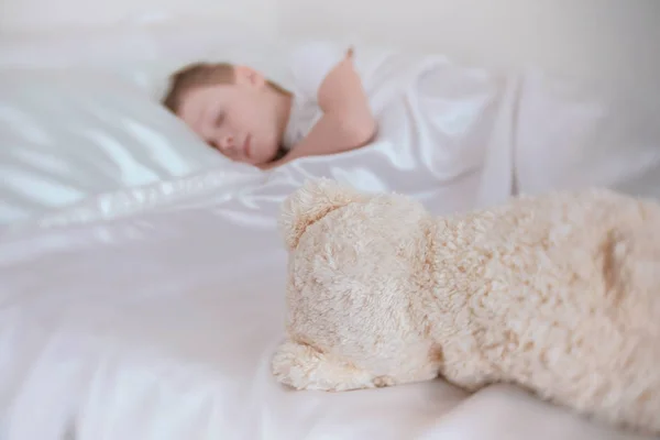 Menino de sete anos adormecendo com urso de brinquedo na cama . — Fotografia de Stock