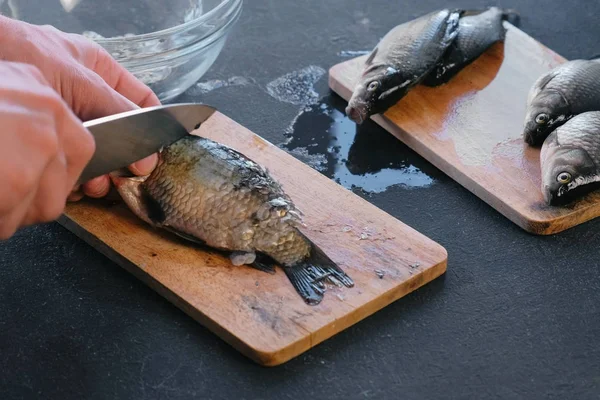 O homem limpa a carpa das escamas. Mãos fechadas. Cozinhar um peixe . — Fotografia de Stock