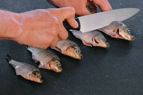 Man makes cuts on carp fish on black table. Cooking fish. Close-up hand.
