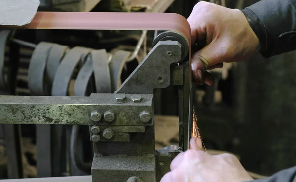 Moagem de tarugos de faca de metal em uma máquina de moagem de cinto. Close-up de uma mão de homem . — Fotografia de Stock