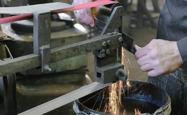 Moagem de tarugos de faca de metal em uma máquina de moagem de cinto. Close-up de uma mão de homem . — Fotografia de Stock