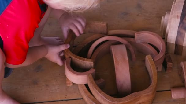 Niño está jugando con la forma de la casa pirámide de juguete de madera de muchos detalles en el suelo de madera. Niño irreconocible . — Vídeos de Stock