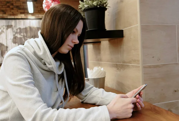 Pensive jovem morena em uma camisa brilhante lê mensagem em seu celular sentado no café . — Fotografia de Stock