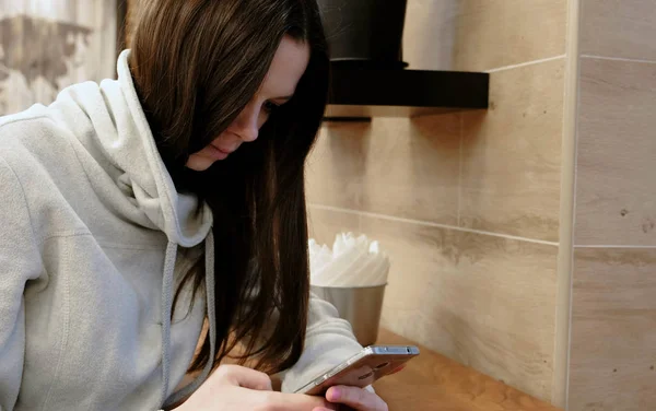 Mujer morena joven pensativa en una camisa brillante trabajando en su teléfono celular sentado en la cafetería . — Foto de Stock