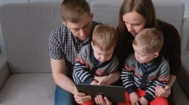 Aile tablet ile. Anne, baba ve iki oğlu ikizler tablet kanepe oturma bakarak.