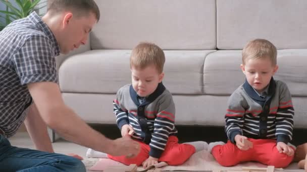Familia mamá, papá y dos hermanos gemelos juegan juntos la construcción de bloques de madera en el suelo . — Vídeos de Stock