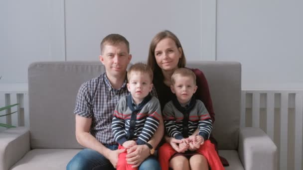 Portrait vidéo de famille de maman, papa et deux jumeaux frères tout-petits. Ils sont assis sur le canapé et regardent la caméra . — Video