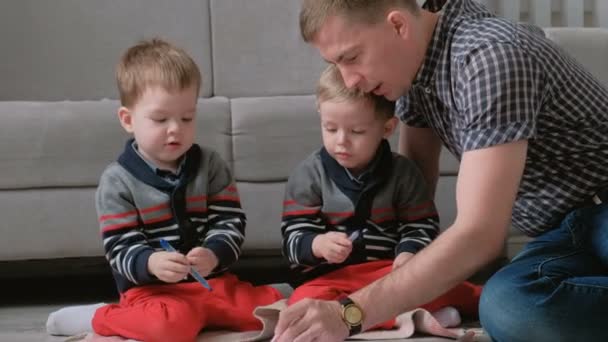 Familienvater und zwei Zwillingsbrüder ziehen Filzstifte und Filzstifte zusammen, die auf dem Boden sitzen. — Stockvideo