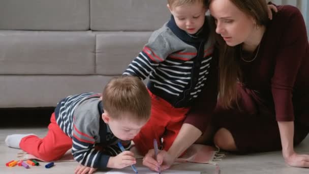 Famiglia mamma e due fratelli gemelli disegnano insieme pennarelli e pennarelli seduti sul pavimento . — Video Stock