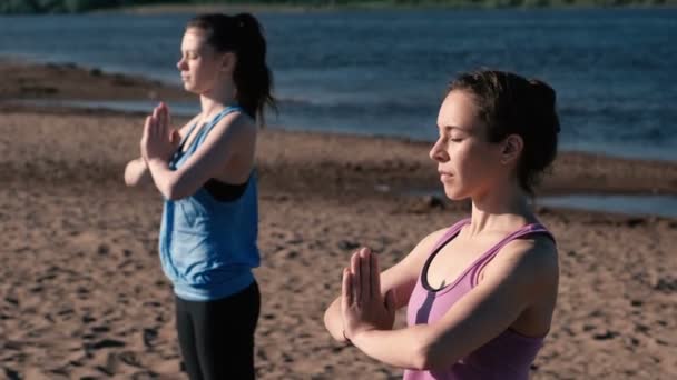 Zwei Frauen dehnen Yoga am Strand am Fluss in der Stadt. schöne Aussicht auf die Stadt. Namaste-Pose. — Stockvideo