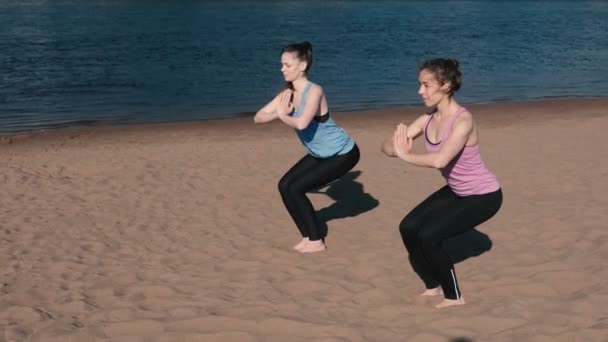 Zwei Frauen beim Yoga am Strand am Fluss in der Stadt. Schöne Aussicht. utkatasana-Pose. — Stockvideo