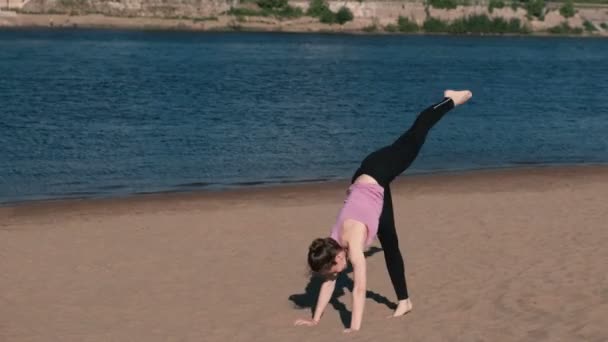 Mujer haciendo yoga en la playa junto al río en la ciudad. Hermosa vista. Soporte de mano . — Vídeos de Stock