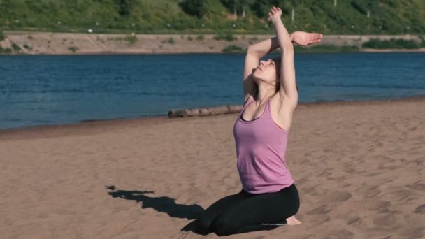 Mujer estirando yoga en la playa junto al río en la ciudad. Hermosa vista de la ciudad. Ejercicio respiratorio . — Vídeos de Stock