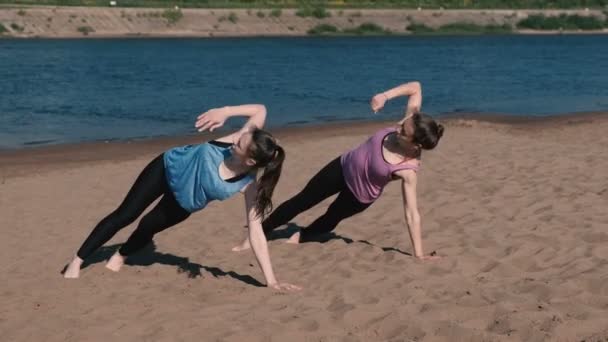 Två kvinna gör övningar sport på stranden av floden i staden. Övningar för händer i plankan. — Stockvideo